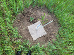 Small garden bed with a square of fabric and a tube in the center, surrounded by grass.