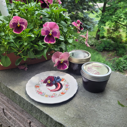 Some jars of Haskap (Honeyberry) jam displayed with a plate and swirl of the jam on it. 